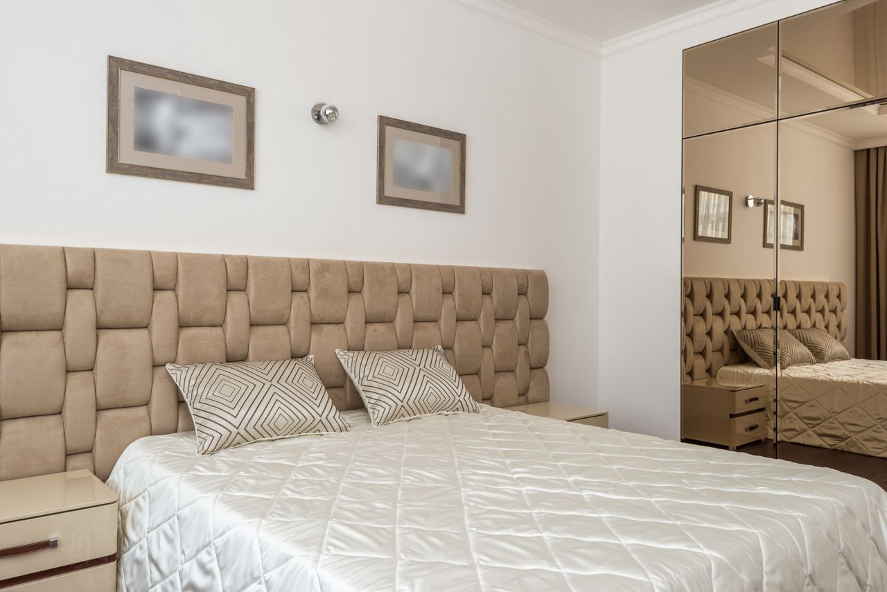 Inviting bedroom with stylish decor, featuring a neutral-toned bed and mirrored closet.